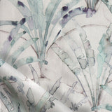 Detail of draped fabric in a painterly palm tree pattern in shades of green and purple on a tan field.