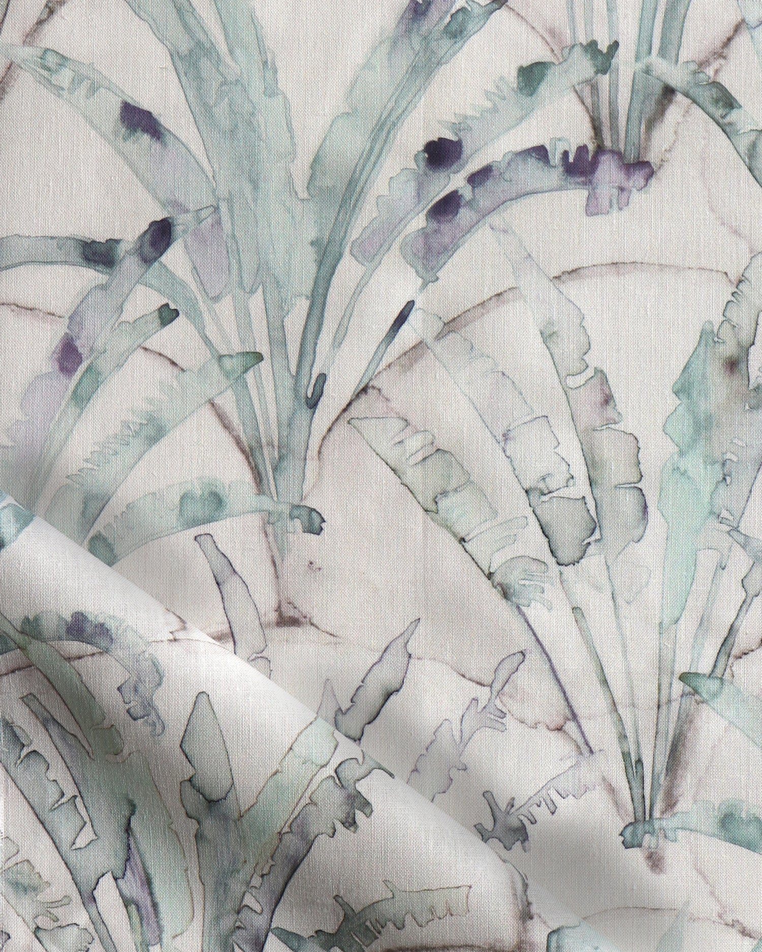 Detail of draped fabric in a painterly palm tree pattern in shades of green and purple on a tan field.