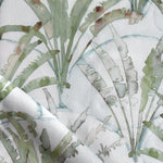 Detail of draped fabric in a painterly palm tree pattern in shades of green and brown on a blue-gray field.