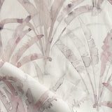 Detail of draped fabric in a painterly palm tree pattern in shades of pink and blue on a cream field.