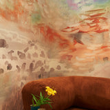 Living room with modernist couch and pendant lamp against ethereal watercolor mural in rust red, warm orange, tan, and taupe.