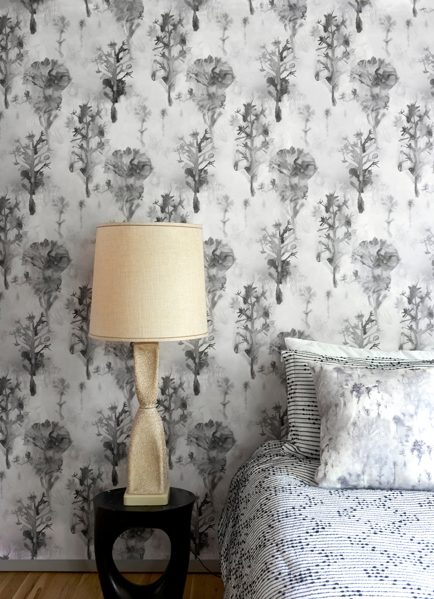 Bedroom scene against a watercolor tree print in shades of gray and black on a white field.