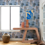 Living room interior with sculptural table and props against a watercolor tree print in shades of turquoise and grey on a blue field. 