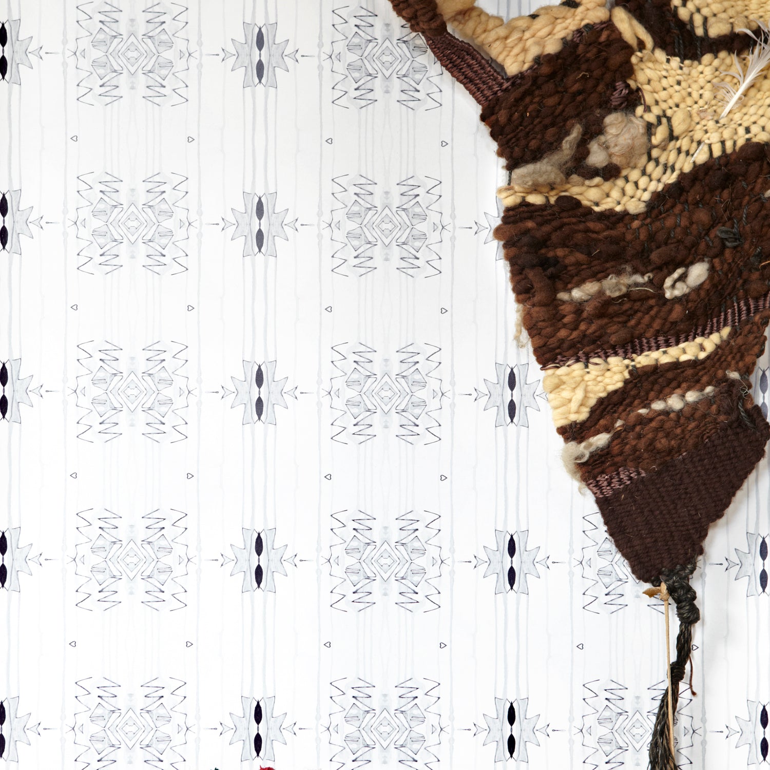 Wallpaper in a minimalist ikat pattern in shades of gray on a white field with a handwoven textile sculpture and woven bench. 