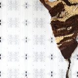 Wallpaper in a minimalist ikat pattern in shades of gray on a white field with a handwoven textile sculpture and woven bench. 