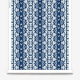 Wallpaper roll in a watercolor ikat stripe print in shades of white and blue on a gray field.