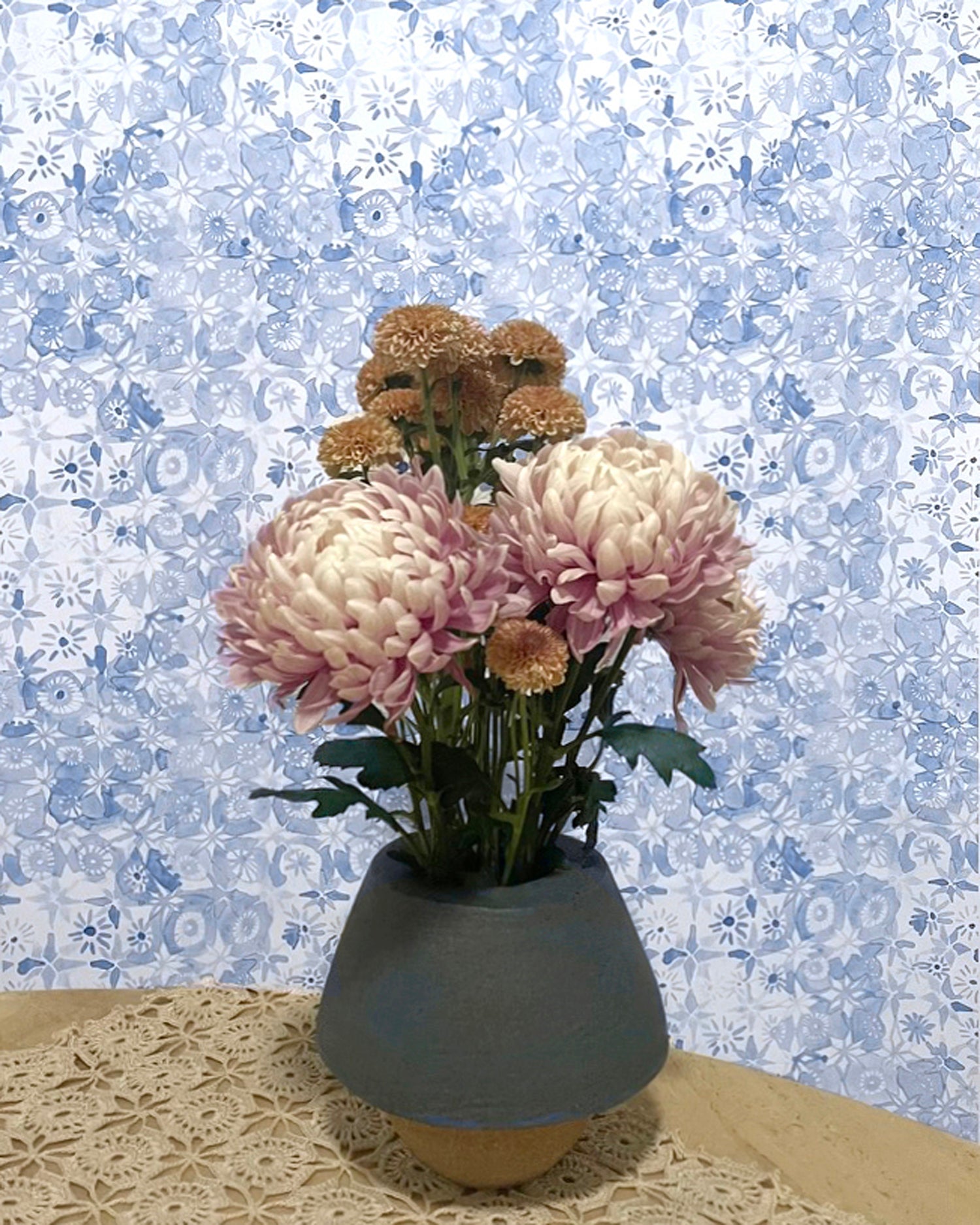 Bouquet of pink and brown flowers in a gray vase against a decorative blue and white patterned wall.