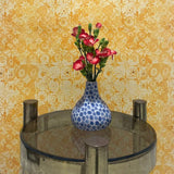 Small round table with a blue polka dot vase and pink flowers against a yellow floral wallpaper.