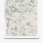 Wallpaper roll in a watercolor branch and floral pattern in grey and blue on a taupe muted taupe field. 