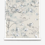 Wallpaper roll in a watercolor branch and floral pattern in grey and blue on a taupe muted taupe field. 