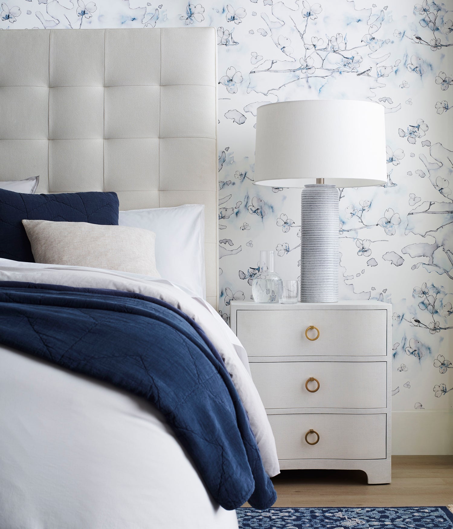Preppy white bedroom scene against wallpaper in watercolor branch and floral pattern in shades of blue on a white field.