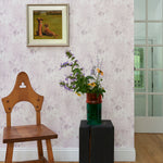 Wallpaper light purple painterly tree pattern framed by wooden chair, side table with flowers and an oil painting. 