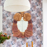 Dining room scene with ornate fringed mirror against painterly tree print wallpaper in turquoise, grey and coral. 