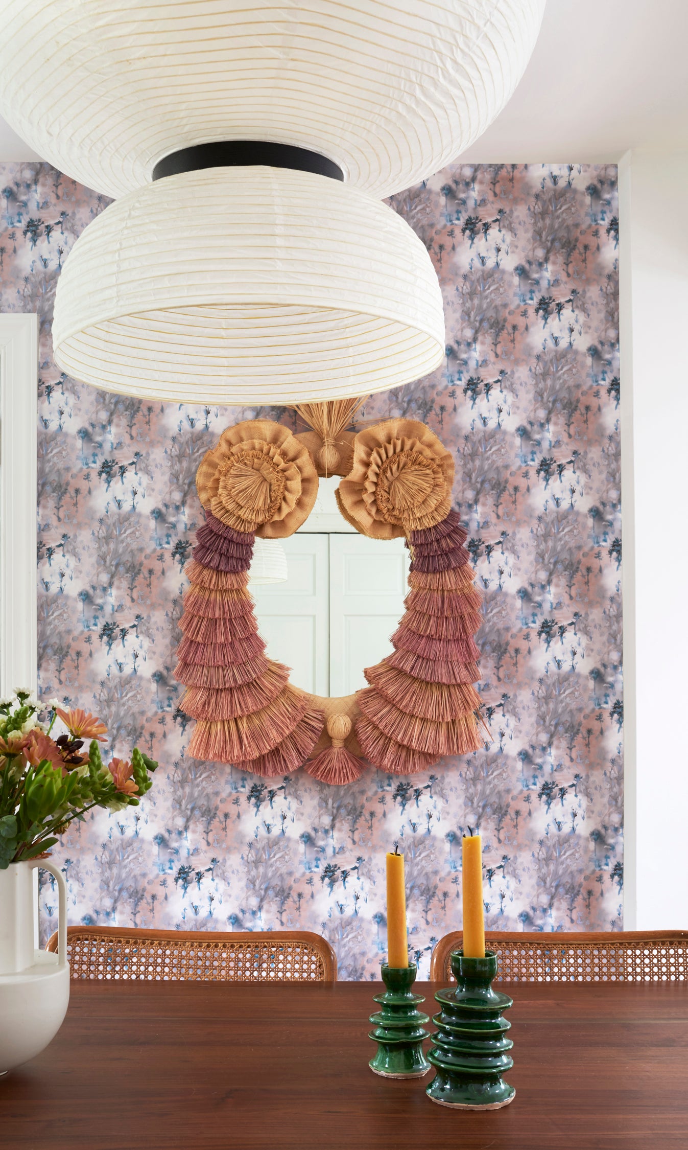 Dining room scene with ornate fringed mirror against painterly tree print wallpaper in turquoise, grey and coral. 