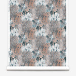 Wallpaper roll in a painterly tree print in light turquoise and gray on a coral field.