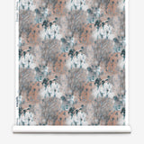 Wallpaper roll in a painterly tree print in light turquoise and gray on a coral field.