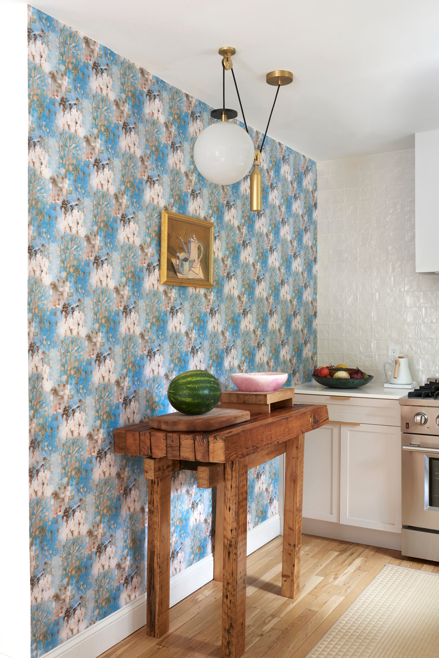 Kitchen scene with a wooden butcher block against wallpaper in a painterly tree print in gray and tan on a turquoise field.
