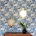 Wooden credenza with paper lantern and props against in a painterly tree print in blue and grey. 