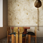 Sculptural wooden table and chairs against wallpaper in abstract floral bushstroke design in warm beige. 