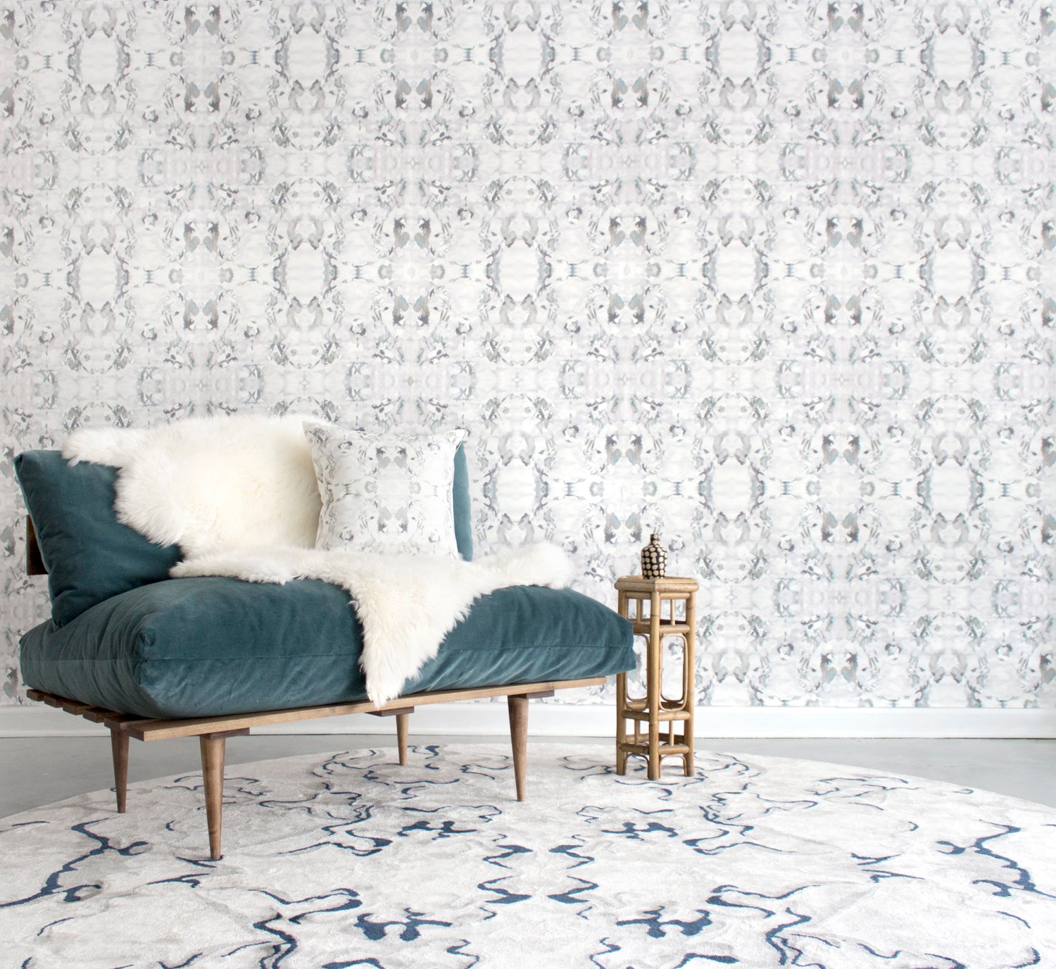 Wallpaper install in a watercolor paint blotch print in gray and turquoise on a white field with a blue velvet couch and white patterned shag rug. 