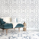 Wallpaper install in a watercolor paint blotch print in gray and turquoise on a white field with a blue velvet couch and white patterned shag rug. 