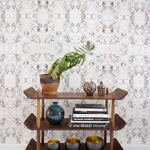 Wallpaper install in a watercolor paint blotch print in purple and gray on a white field with a wooden bookshelf with accessories.