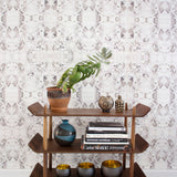 Wallpaper install in a watercolor paint blotch print in purple and gray on a white field with a wooden bookshelf with accessories.