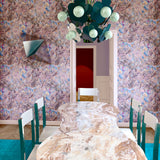 Dining room with sculptural table, chairs and light fixture wallpapered in a painterly tree print in pink, orange, gray and blue.