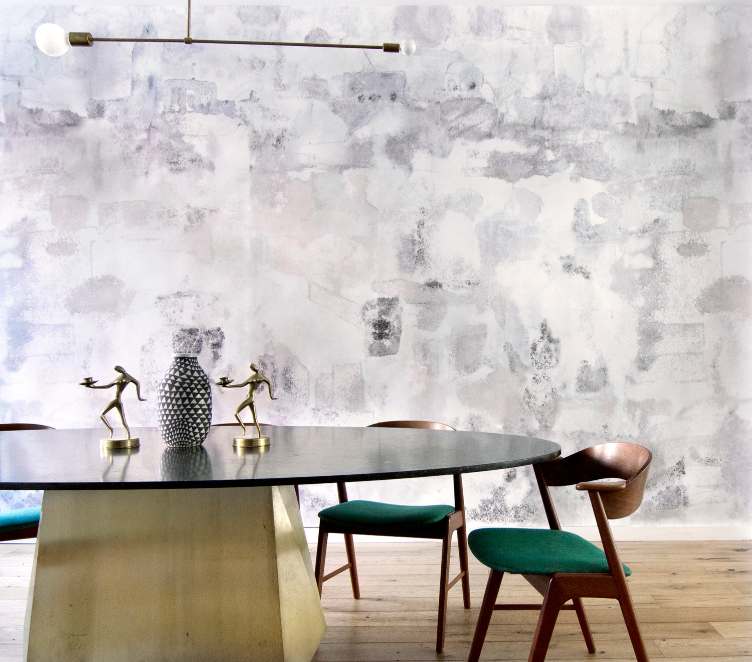 Dining room table and chairs against wallpaper mural in a minimal splatter print in shades of gray on a cream field.
