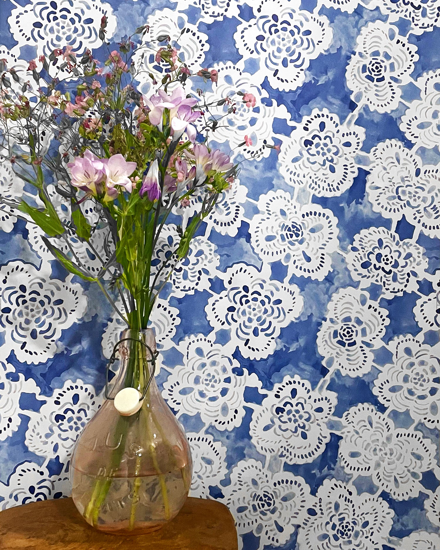 Vase with flowers against a blue wall with white lace patterns