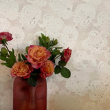Vase shaped like a face with flowers on top of books against a patterned wall.