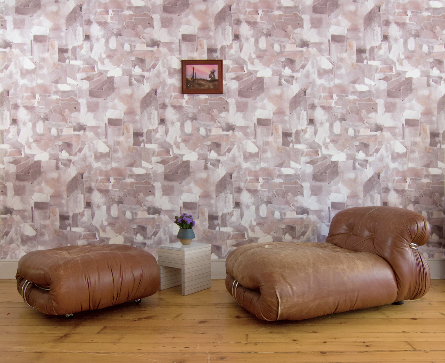 Modern camel leather accent chair against wallpaper in a textural paint blotch print in shades of brown and tan on a white field.