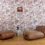 Modern camel leather accent chair against wallpaper in a textural paint blotch print in shades of brown and tan on a white field.