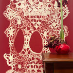 Decorative lace wallpaper in red with a vase on a wooden surface.