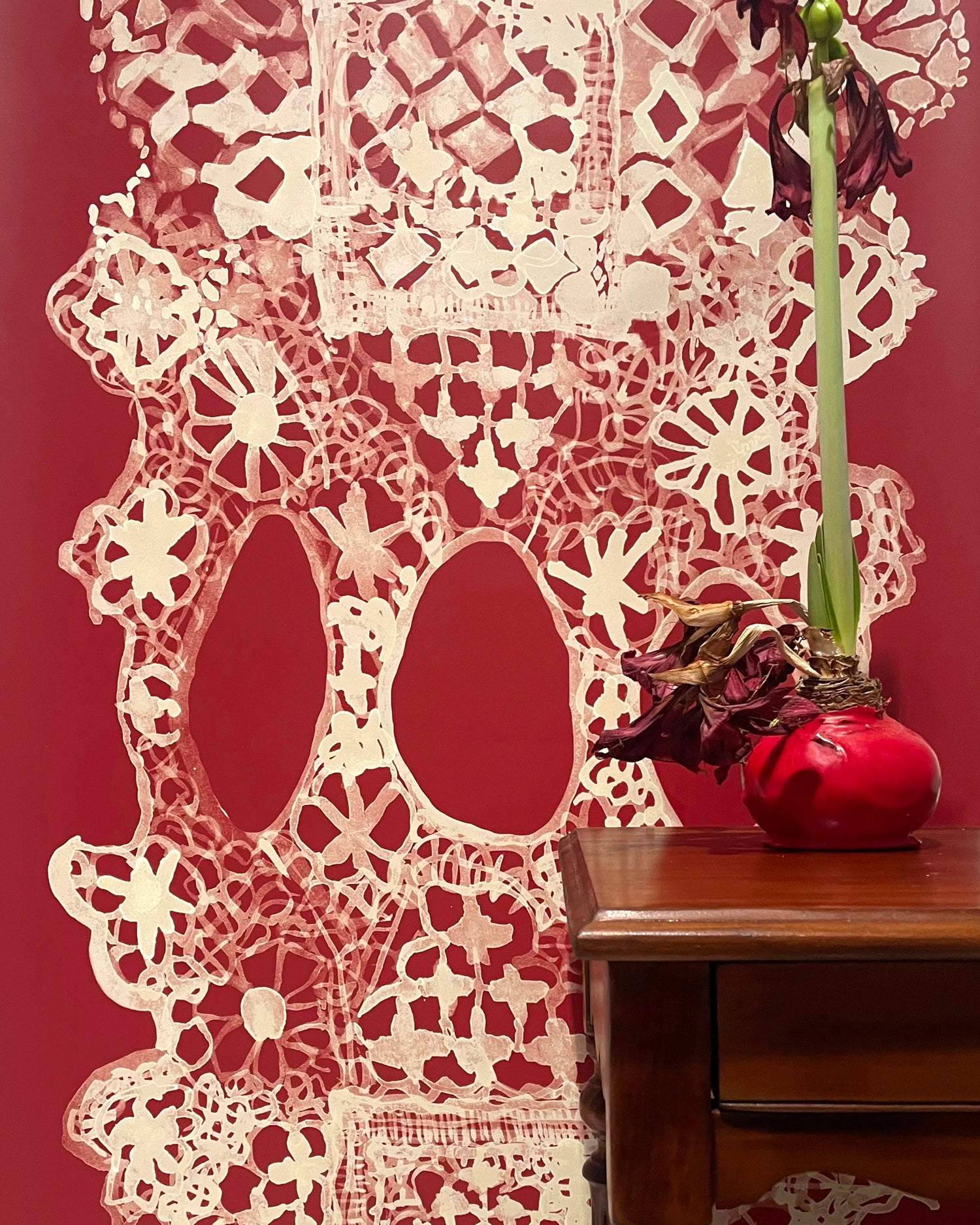 Decorative lace wallpaper in red with a vase on a wooden surface.