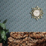 Retro couch in mottled brown with a potted plant against wallpaper in  an undulating abstract watercolor motif in shades of steel blue and charcoal. 