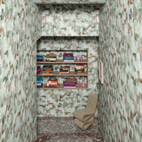 Stone staircase down to a landing with chair and built in book case surrounded by green abstract puzzle wallpaper. 