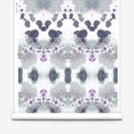 Wallpaper roll in a watercolor inkblot print in shades of purple and gray on a cream field.