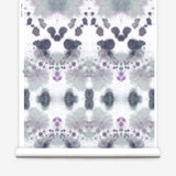 Wallpaper roll in a watercolor inkblot print in shades of purple and gray on a cream field.