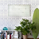 Living room with a white shag rug, dog, and low bookshelf against wallpaper in a watercolor inkblot print in shades of blue-gray on a cream field.