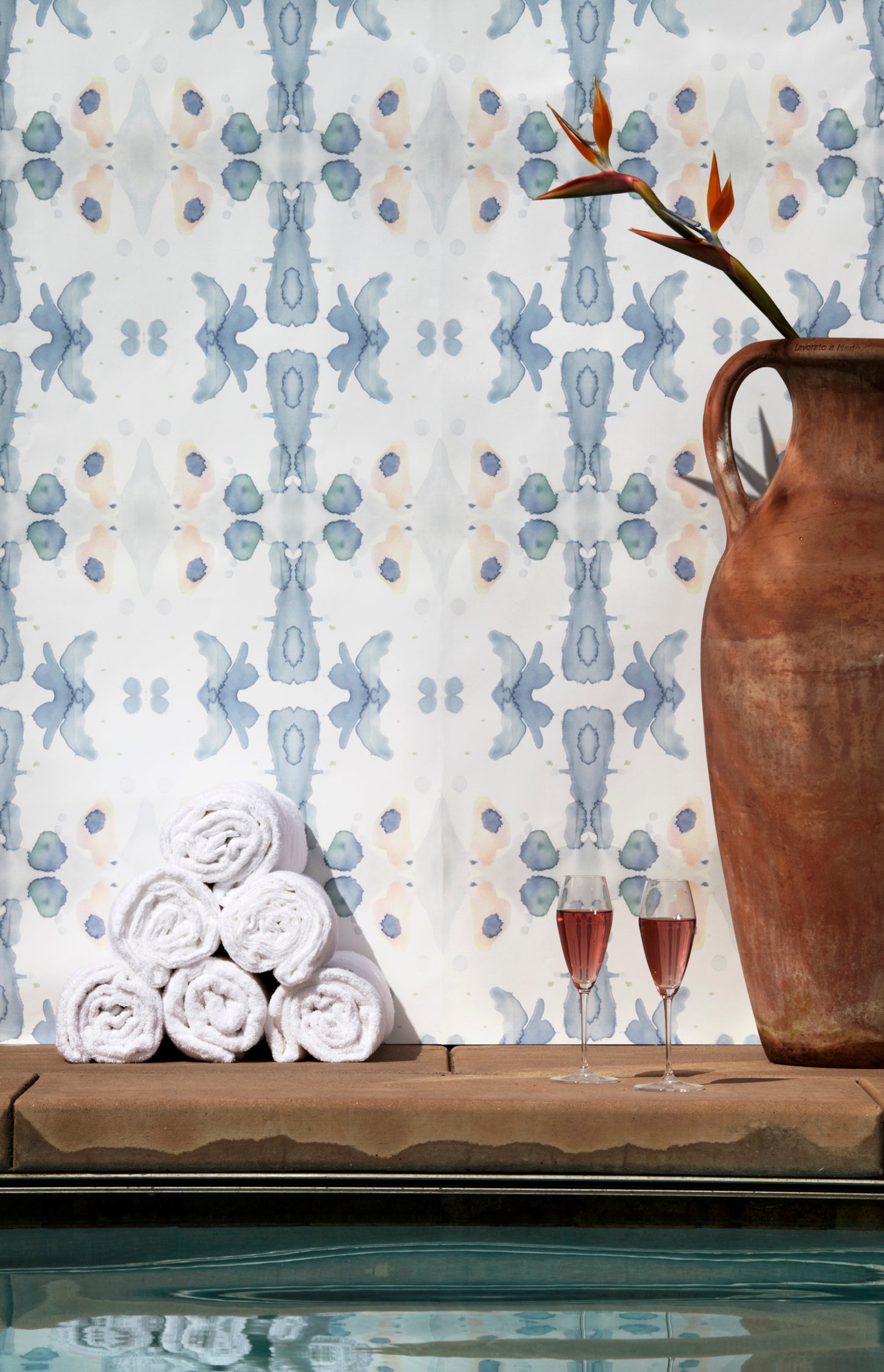 Wallpaper installed behind a plunge pool with props in a watercolor ink splash print in shades of pastel blue and pink on a cream field.