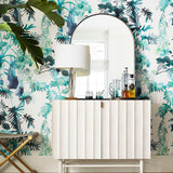 White fluted credenza with bottles and mirrors against a green palm frond wallpaper. 
