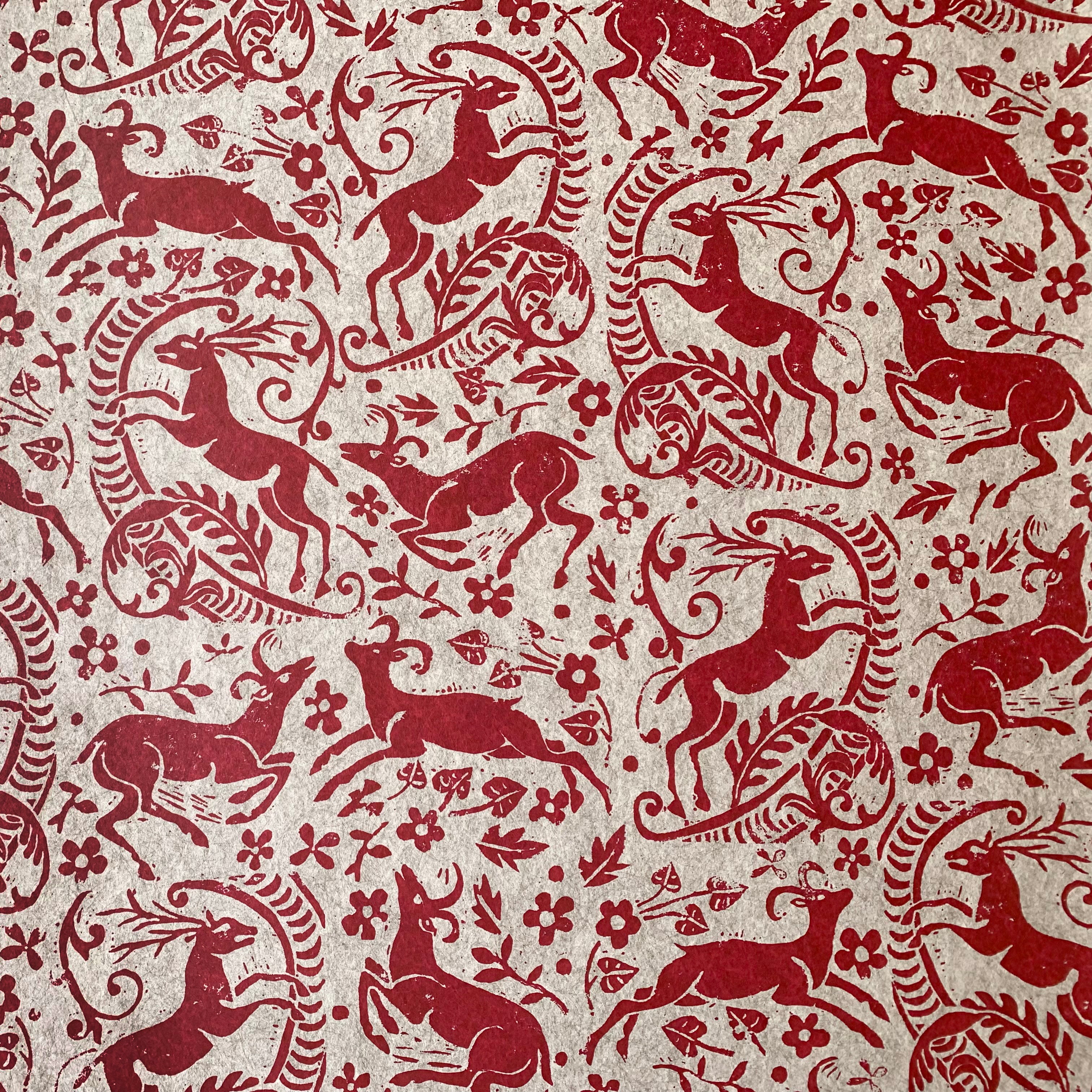Detail of wallpaper in a deer, leaf and flower print in red on a mottled beige field.