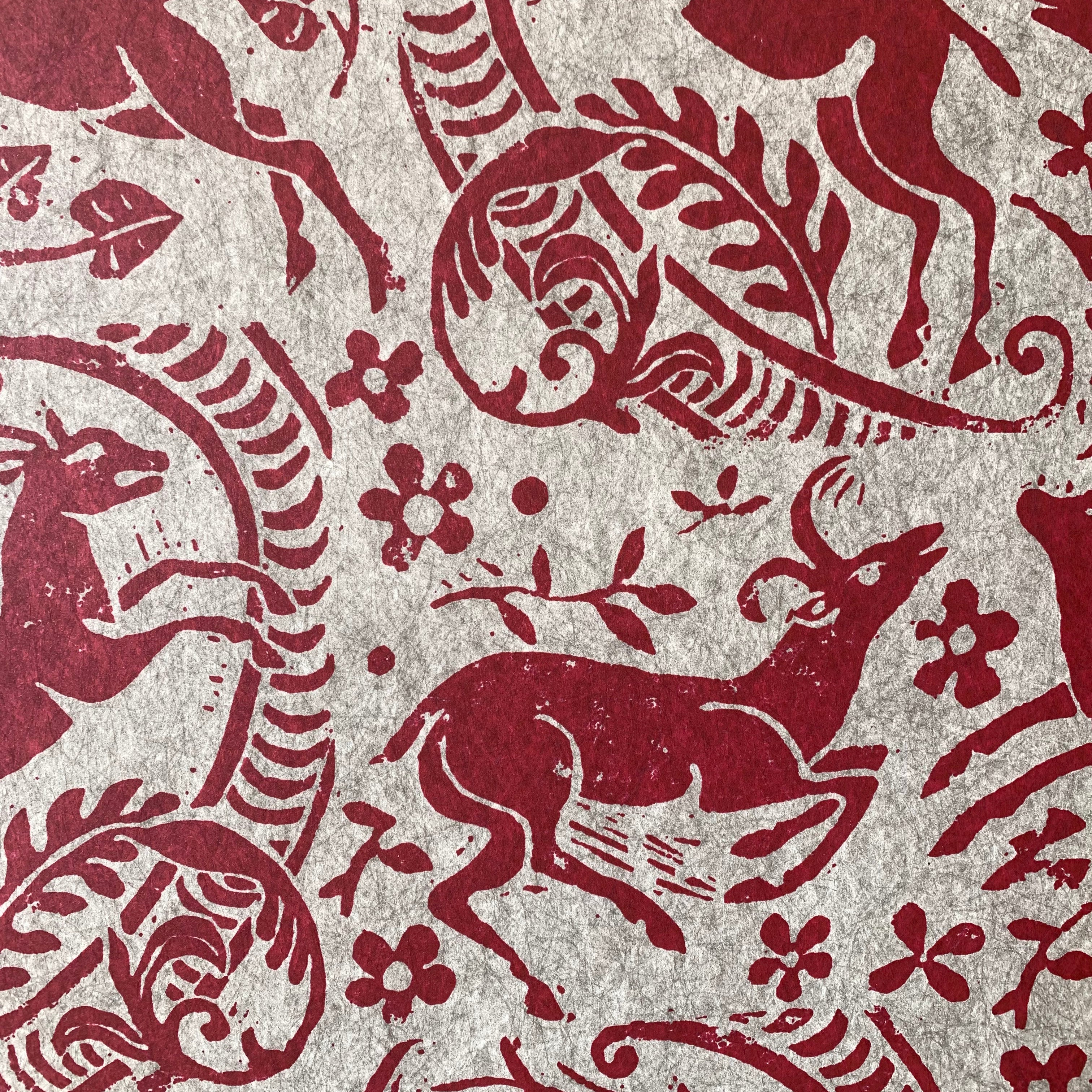 Close-up of wallpaper in a deer, leaf and flower print in red on a mottled beige field.