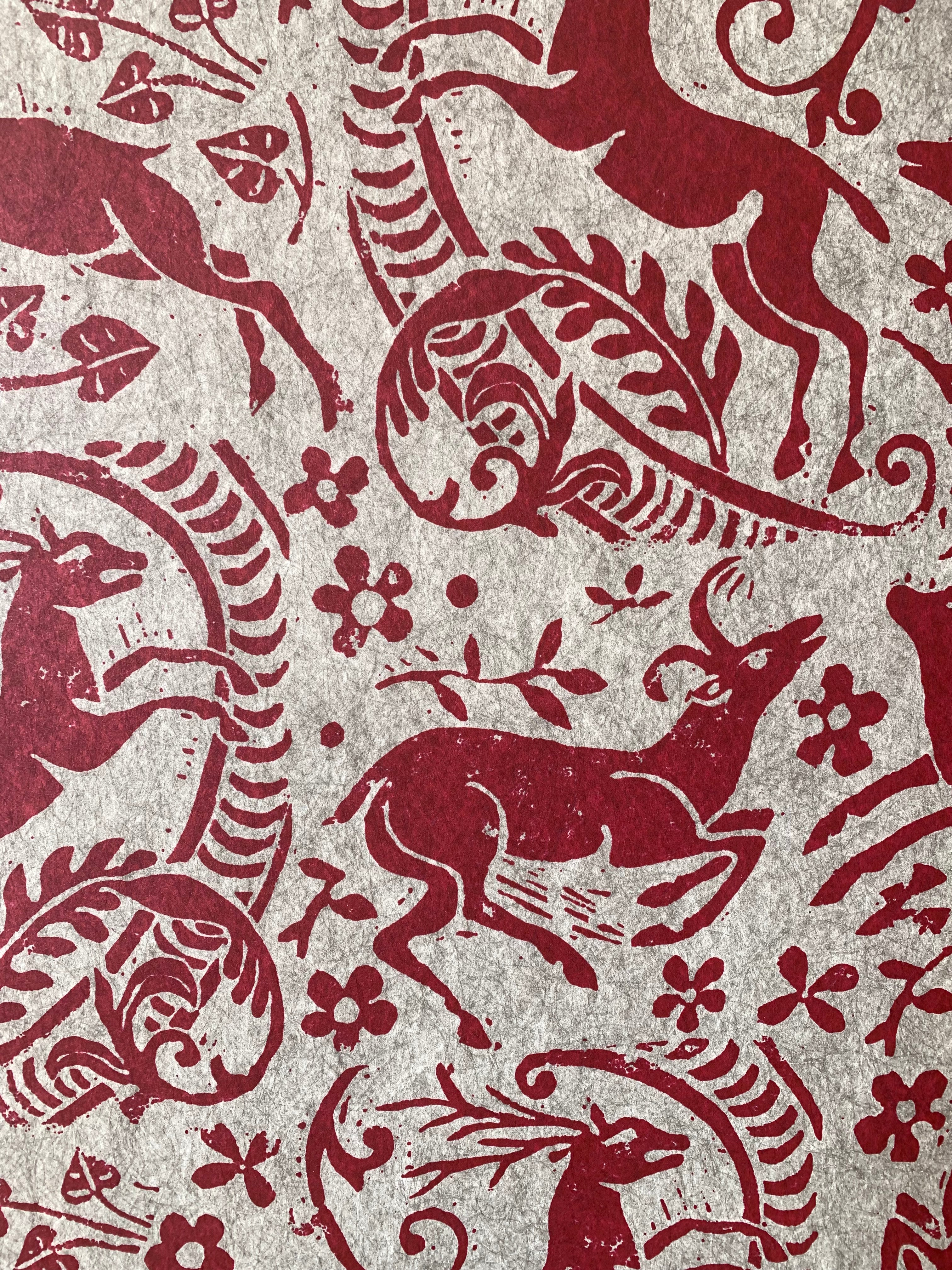 Close-up of wallpaper in a deer, leaf and flower print in red on a mottled beige field.