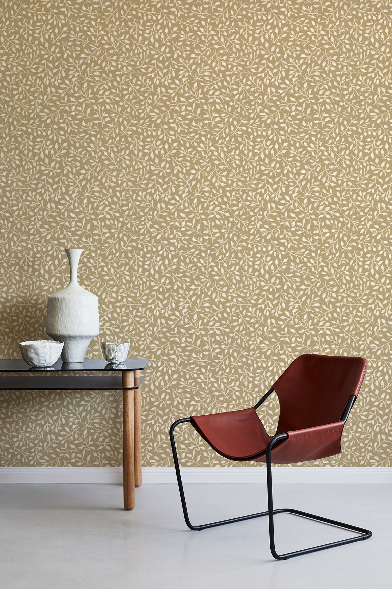 Modern interior with a red chair, table, and decorative items against a leaf patterned wall.