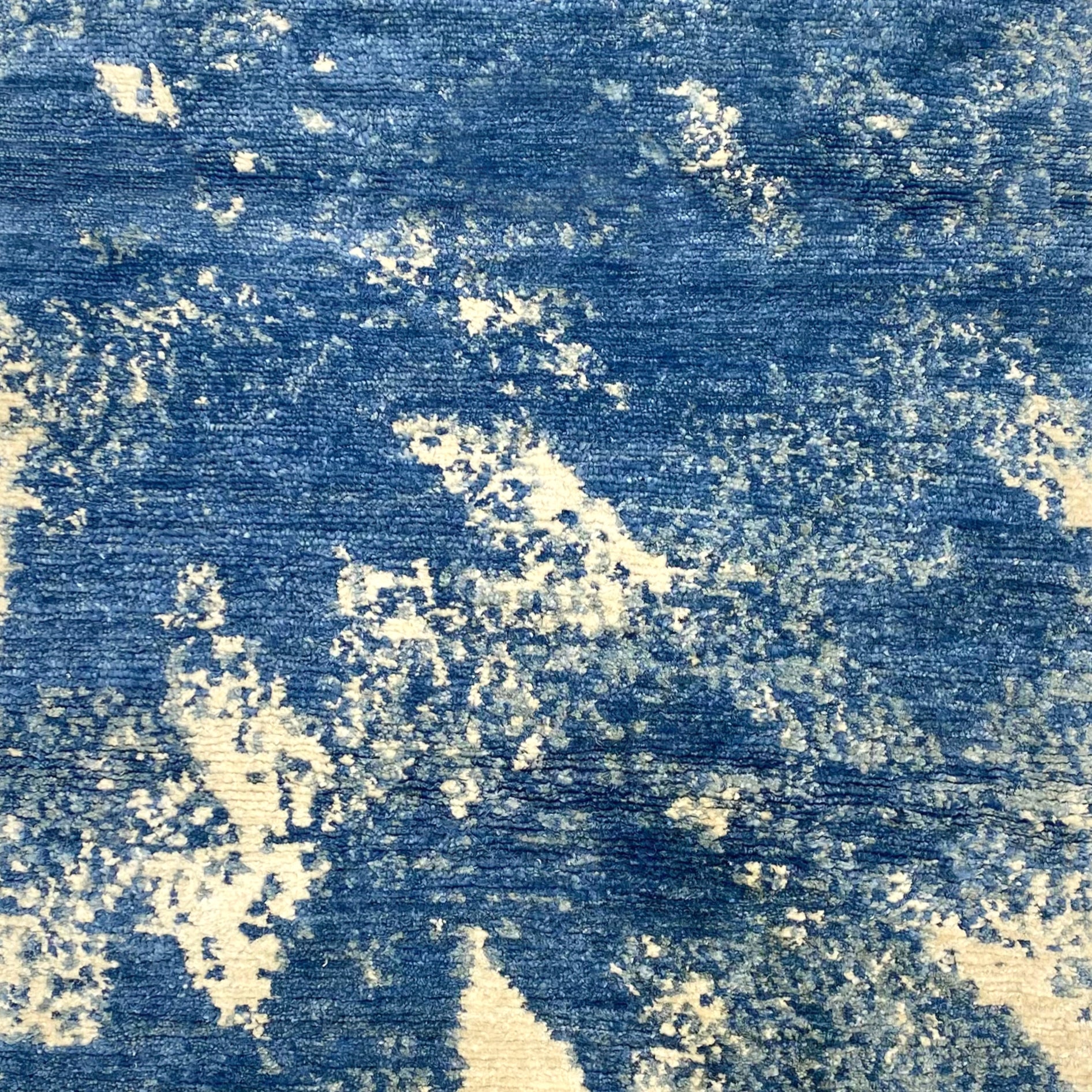 Handknotted rug sample in an abstract texture in blue with accents of cream. 