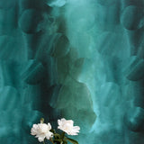 A vase of flowers stands in front of a wall papered in an abstract curvilinear pattern in mottled turquoise and black.