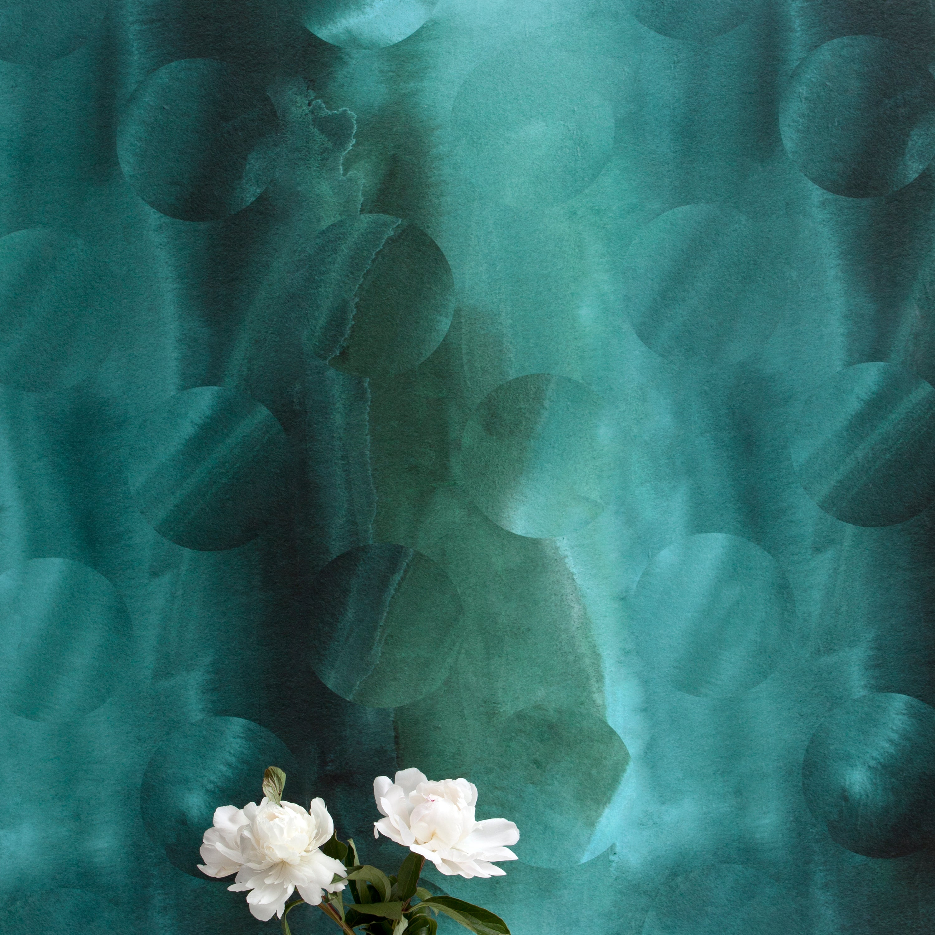 A vase of flowers stands in front of a wall papered in an abstract curvilinear pattern in mottled turquoise and black.