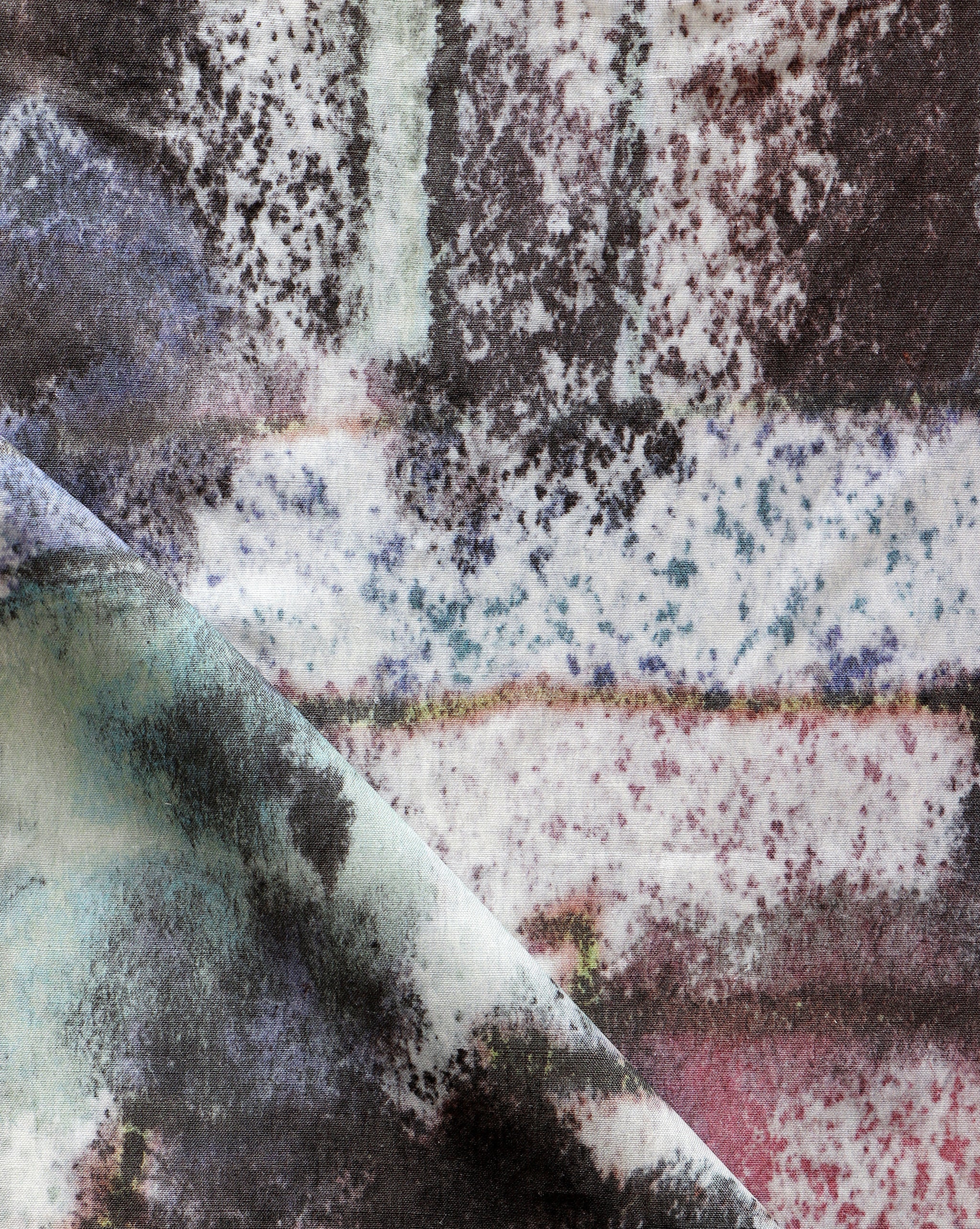 Detail of fabric in a minimal splatter print in shades of green, brown and pink on a cream field.